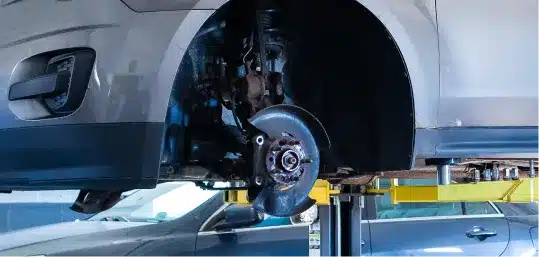 Close-up of a car’s exposed wheel hub and brake assembly on a hydraulic lift.