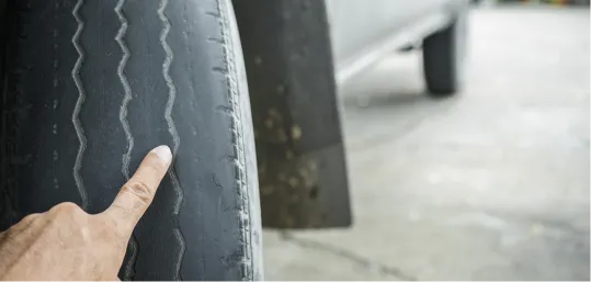 Finger pointing at a worn-out tire tread on a vehicle.