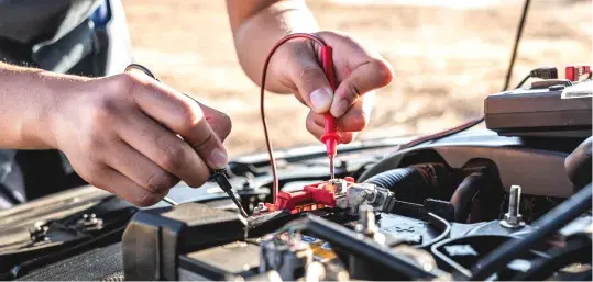 Mechanic testing a car battery with a multimeter. Close-up on hands and battery terminals.