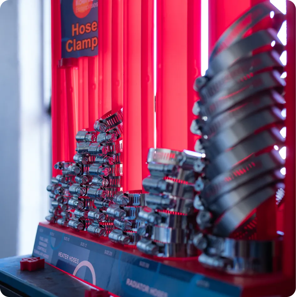 A display of Koehler Enterprises KEDIS220 220 Piece Hose Clamp Set is shown with various sizes of silver metal hose clamps arranged on a blue and red stand. A sign above reads "Hose Clamp." The clamps are organized in rows, and the display is illuminated with red lighting. Labels on the stand indicate "HEATER HOSES" and "RADIATOR HOSES."