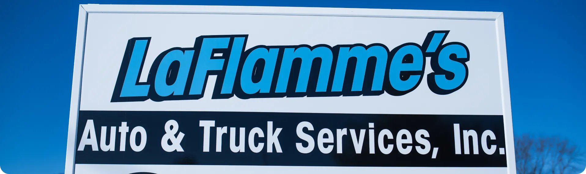 state inspection, auto & truck services in Westfield, MA at LaFlamme's Auto & Truck Services. A sign with a white background and a blue and black logo for "LaFlamme's Auto & Truck Services, Inc." is shown against a clear blue sky. The name "LaFlamme's" is in a stylized blue font with a black outline, while "Auto & Truck Services, Inc." is in a simpler white font on a black rectangular background.